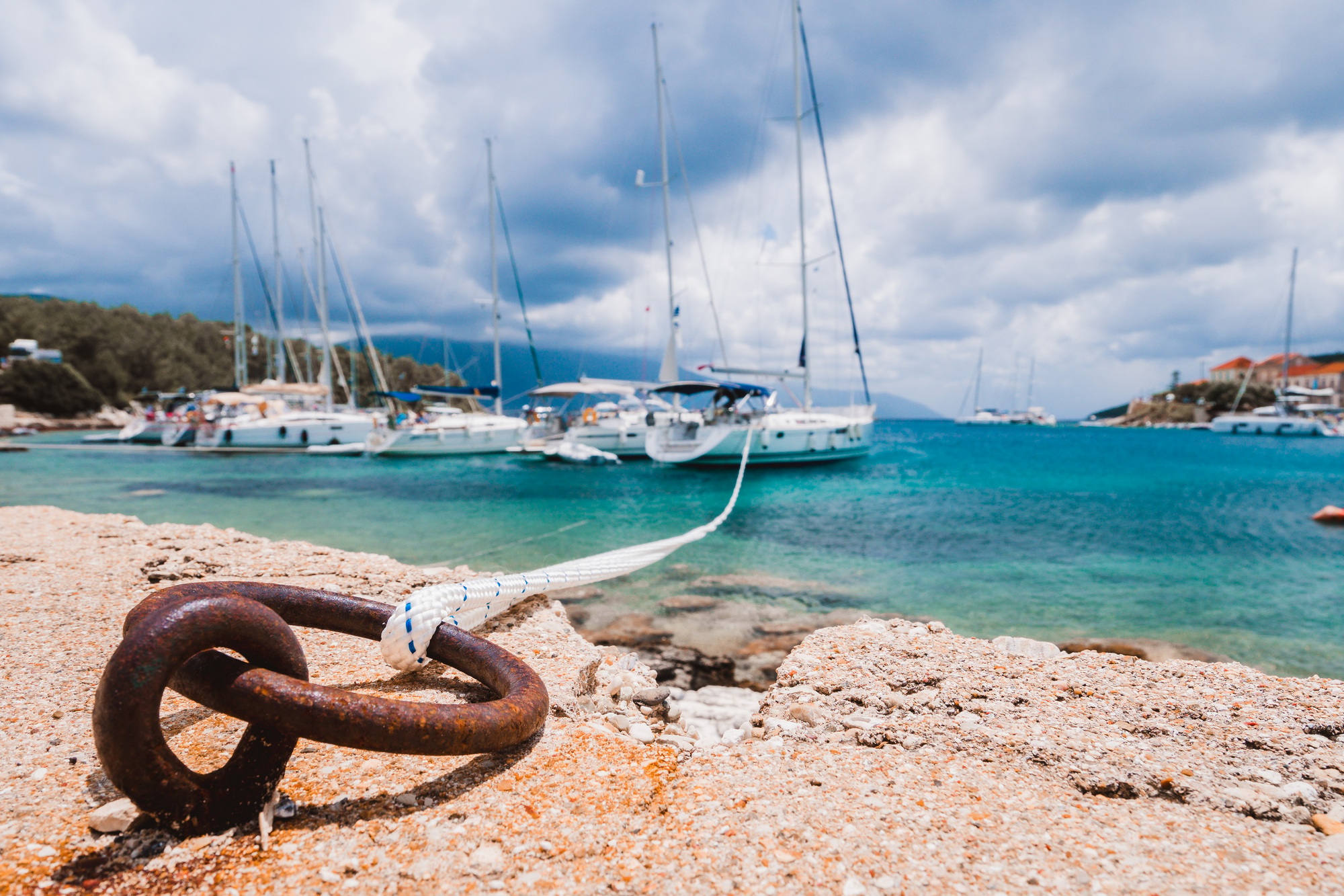 Mooring rope tied to rusty ring for rigging yachts in background. Wonderful view of port Fiskardo